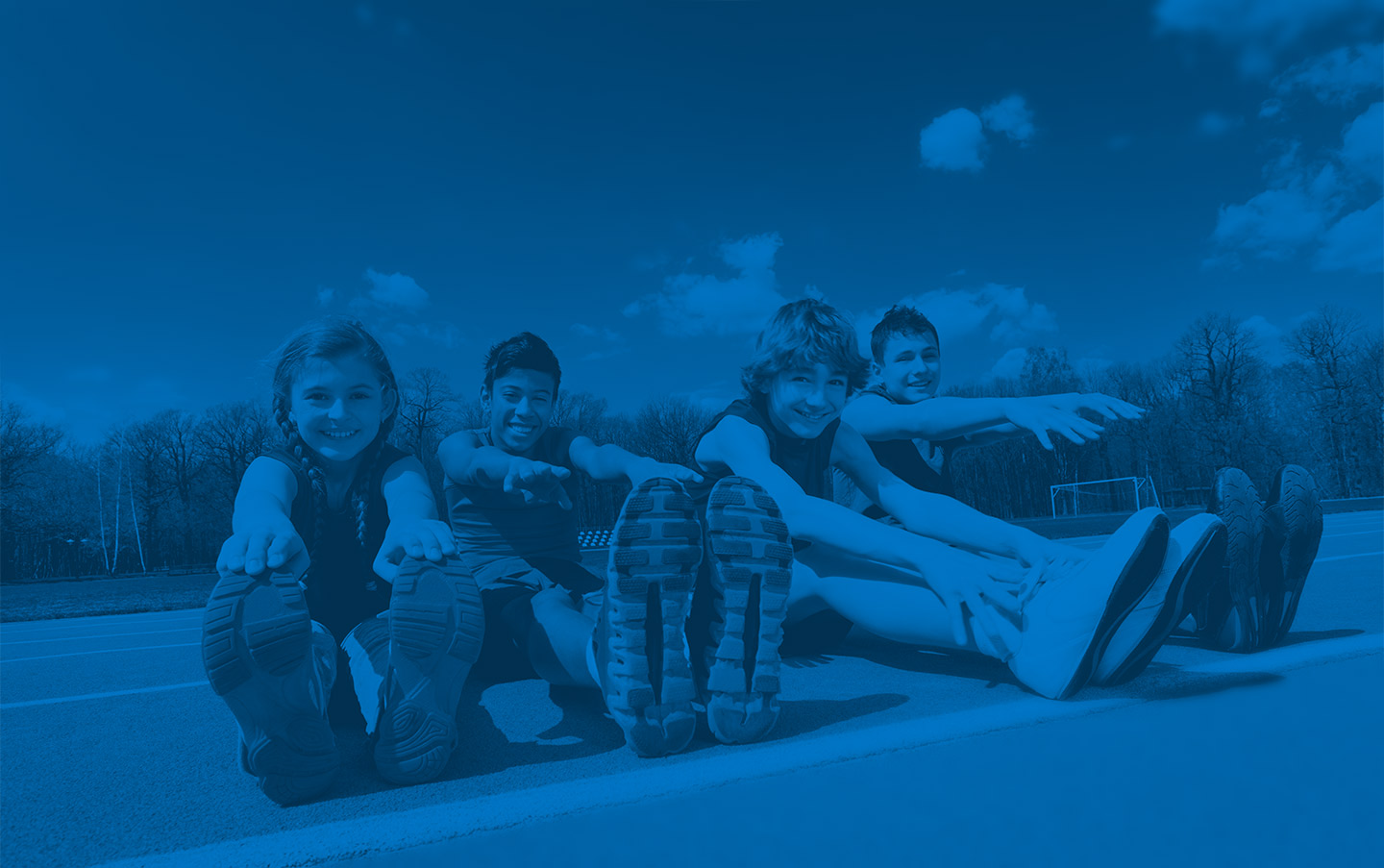 Image of kids sitting on a race track stretching to touch their toes
